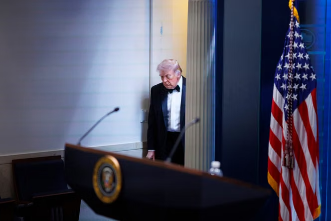 Donald Trump près d’un pupitre présidentiel, un drapeau américain en arrière-plan.